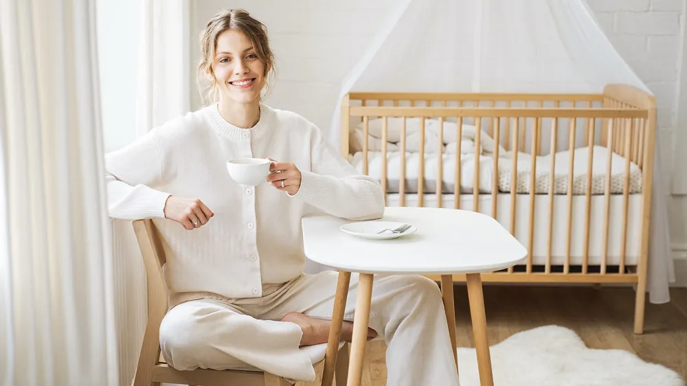 Mama kilka miesięcy po porodzie w jasnej sypialni przy łóżeczku dziecka